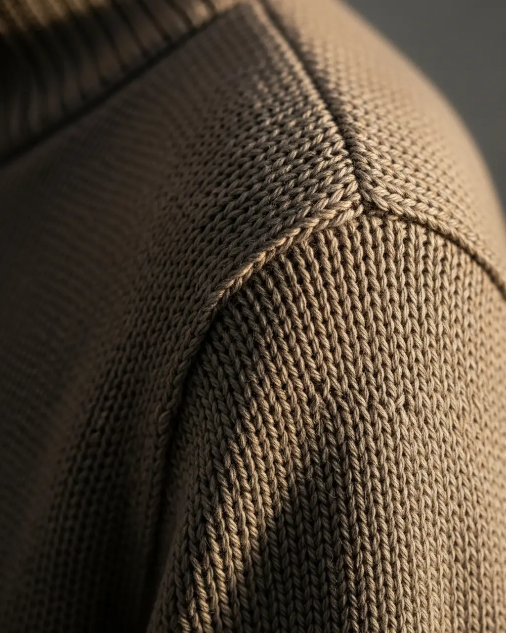 Macro close-up of tight fine-gauge merino wool knit stitches and a fully-fashioned shoulder seam showing construction quality