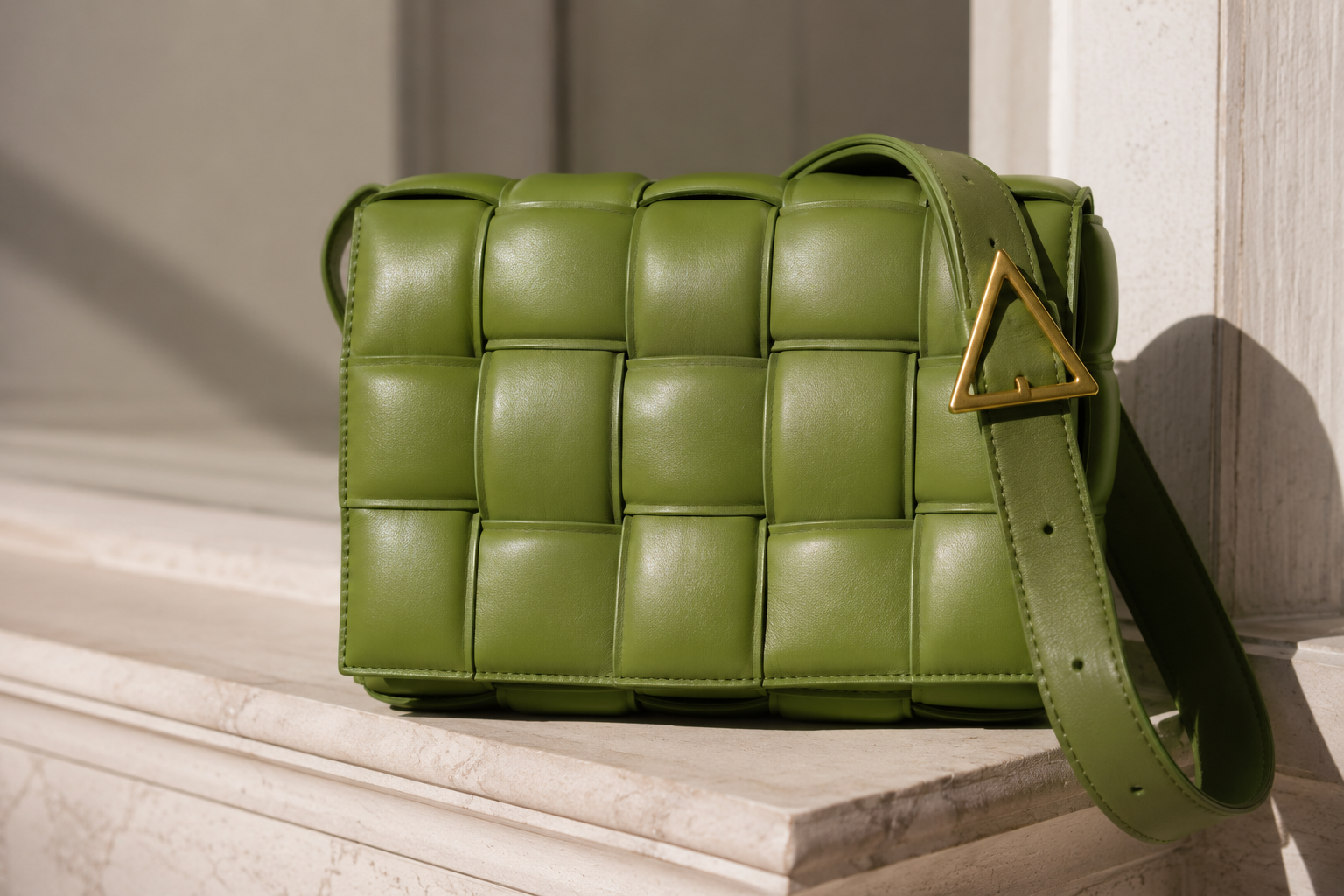 Close shot of a padded Bottega Veneta Cassette intrecciato shoulder bag in parakeet green resting on a pale marble ledge in soft daylight